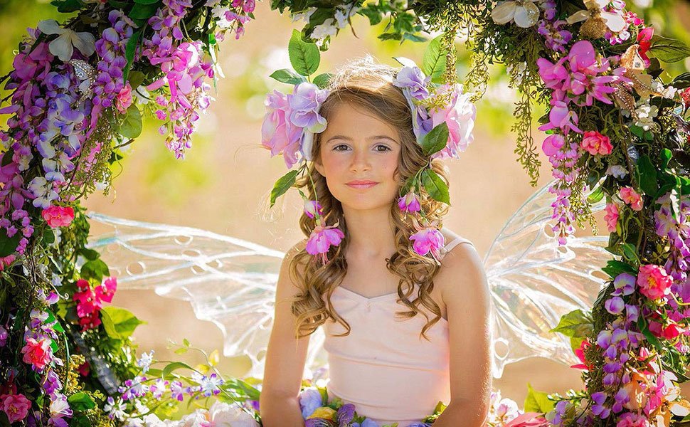 Young girl with fairy wings and flower crown sits amidst floral decorations