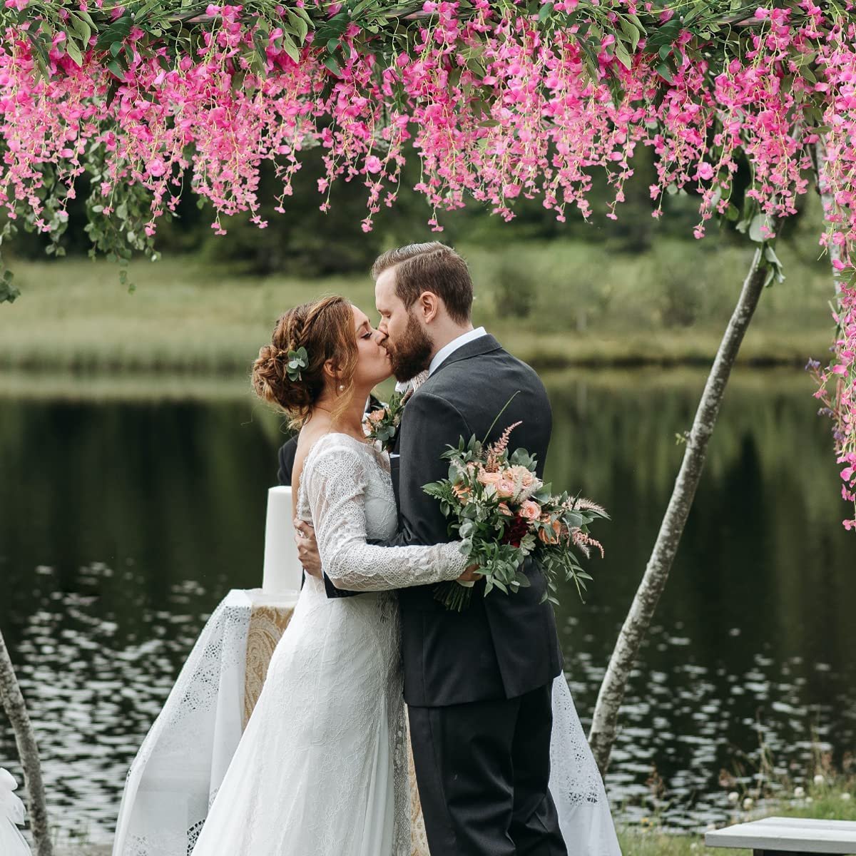 Couple kissing under a floral archway with pink wisteria flowers at an outdoor wedding ceremony