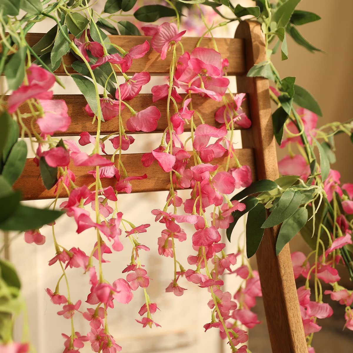 Close-up of fuchsia artificial wisteria garlands draped over a wooden chair back.