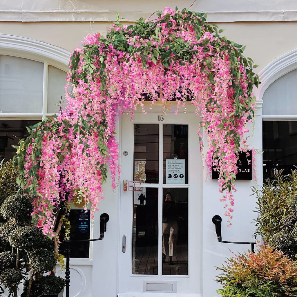 Artificial fuchsia wisteria garlands draped over a white doorway and archway, with green leaves and pink flowers cascading down.