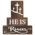 Three stacked wooden blocks with Christian Easter message 'HE IS Risen' and three crosses on the top block.