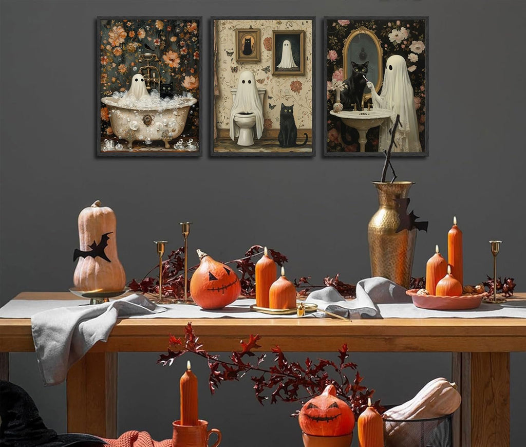Three Halloween-themed canvas art prints featuring ghosts and black cats in a bathroom setting, displayed above a table with pumpkins and candles.