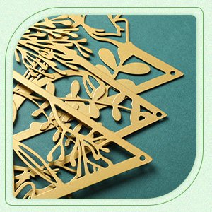 Close-up of three gold metal floral wall art pieces with intricate cutouts, arranged in a stack against a teal background.