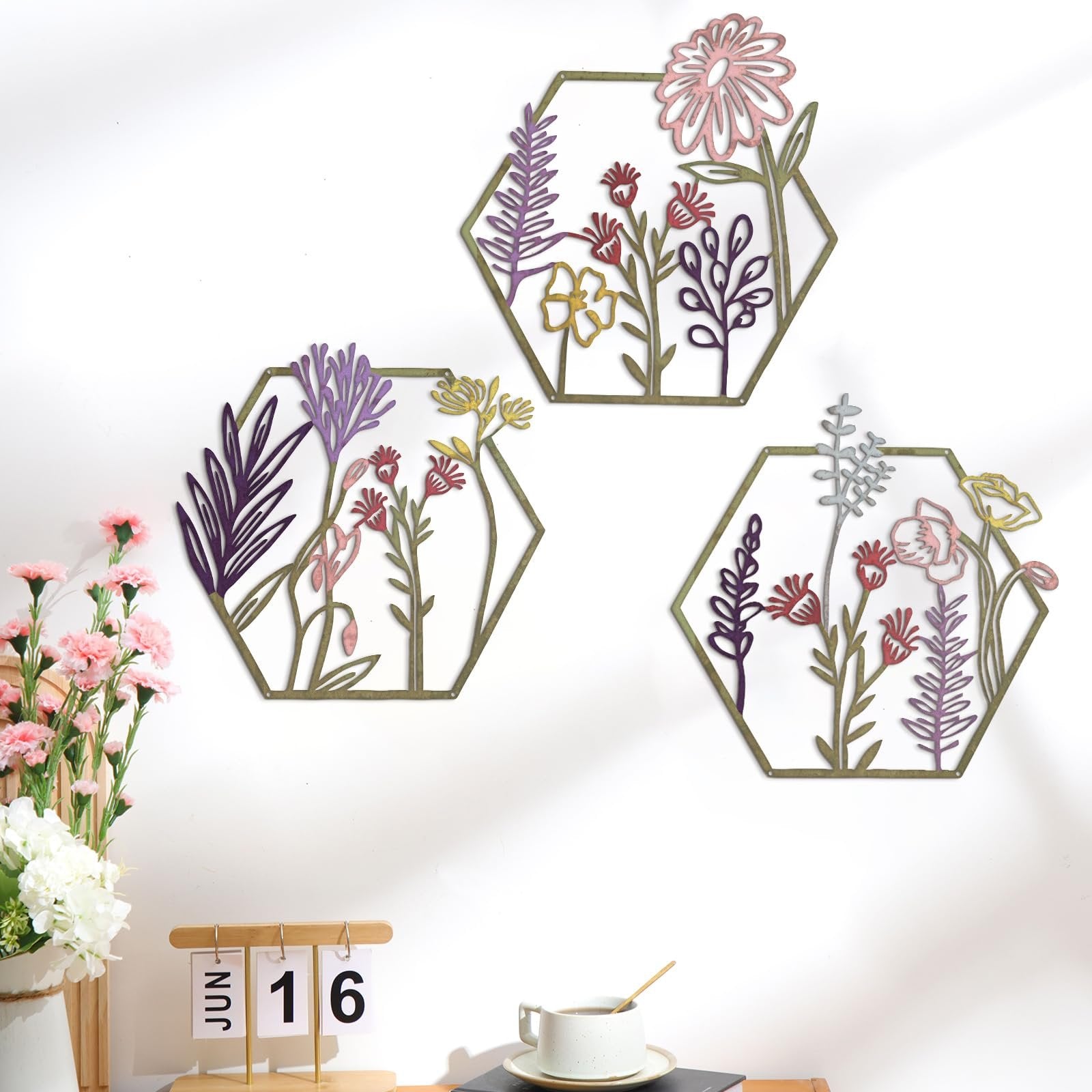 Three hexagonal metal wall art pieces featuring colorful floral and botanical designs, displayed on a white wall.