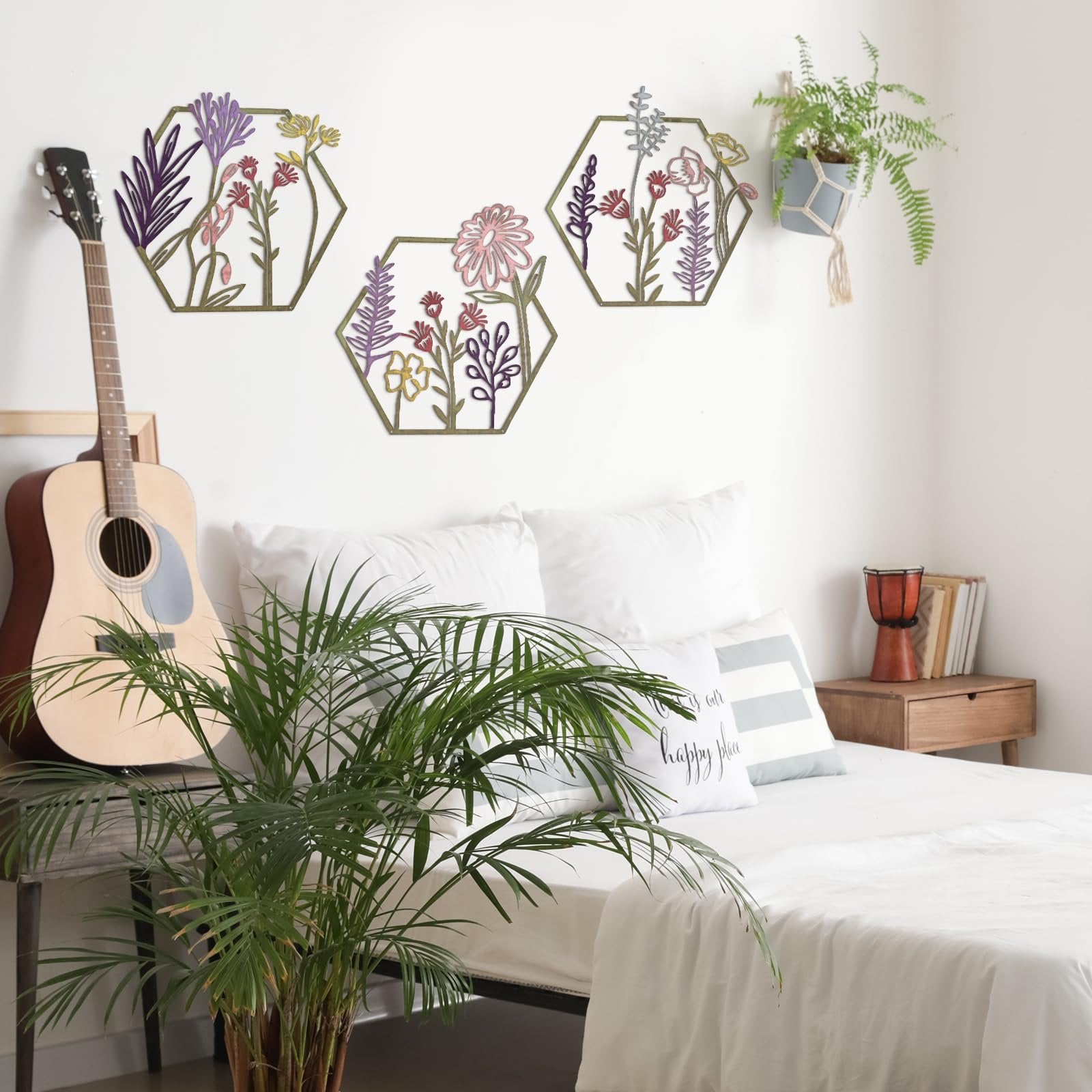 Three hexagonal metal flower wall decor pieces with colorful floral designs hanging on a white wall above a bed.