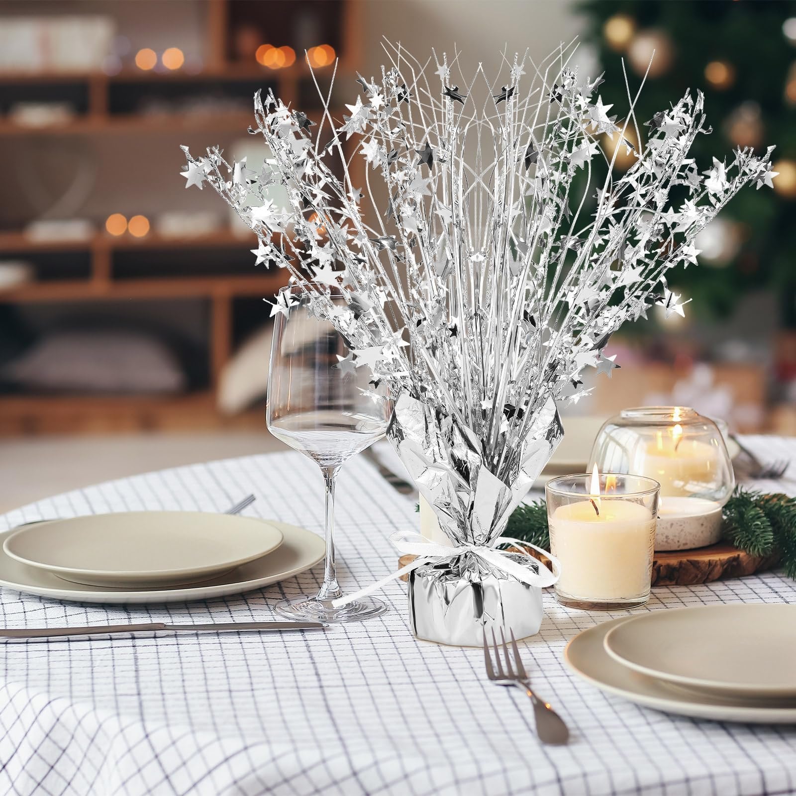 Silver metallic star burst table centerpiece on a set table with plates and wine glass, with candles and greenery in the background.