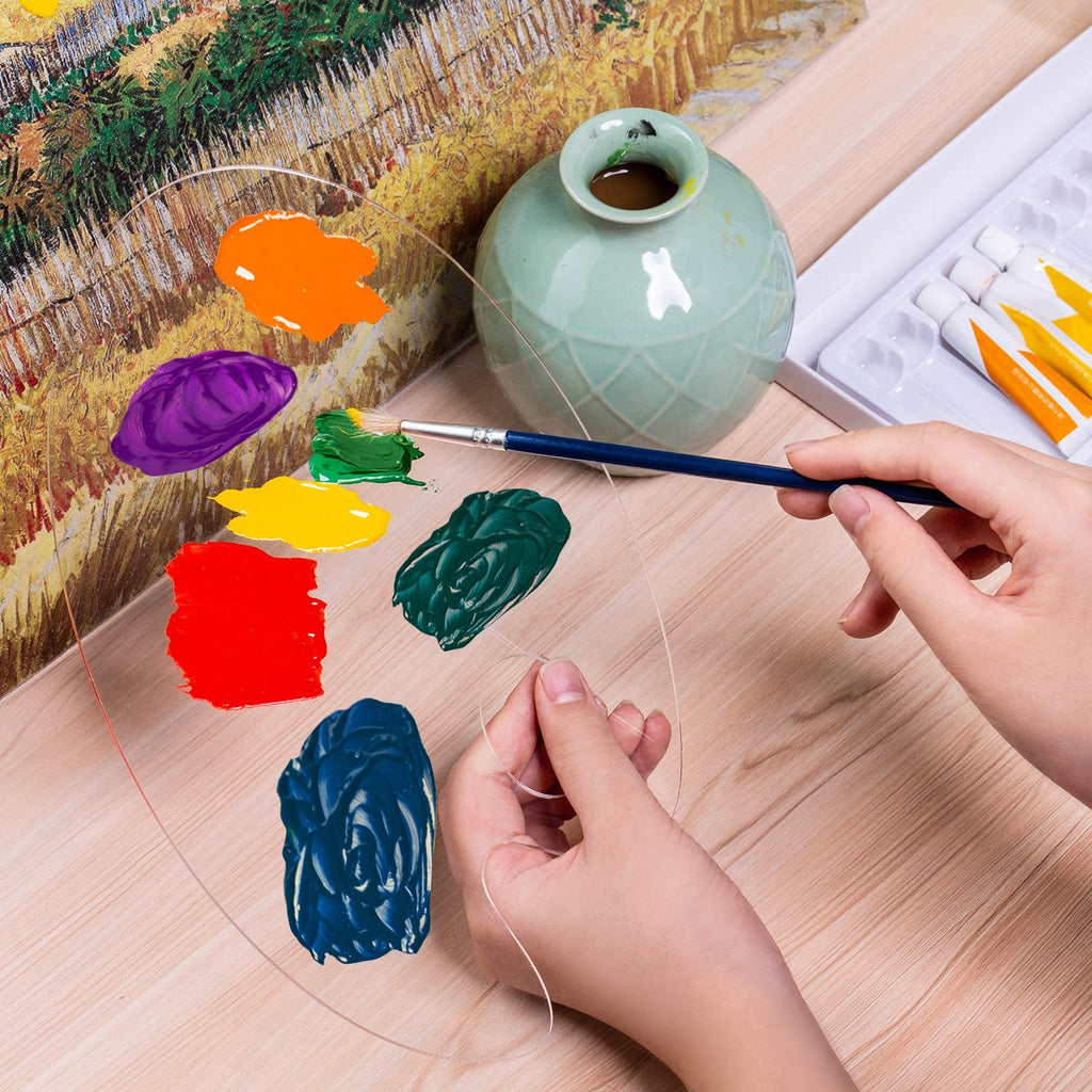 Hands mixing colorful paints on a clear acrylic palette next to a vase and a painting.