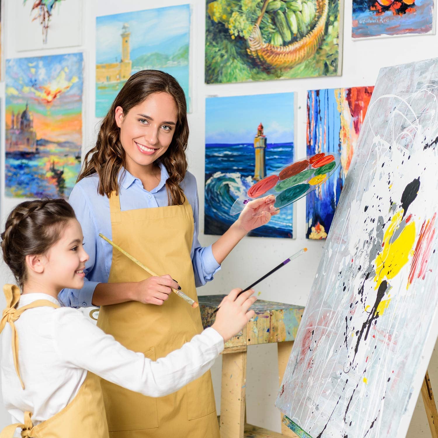 Woman and child painting together in an art studio, holding paint palettes and brushes.