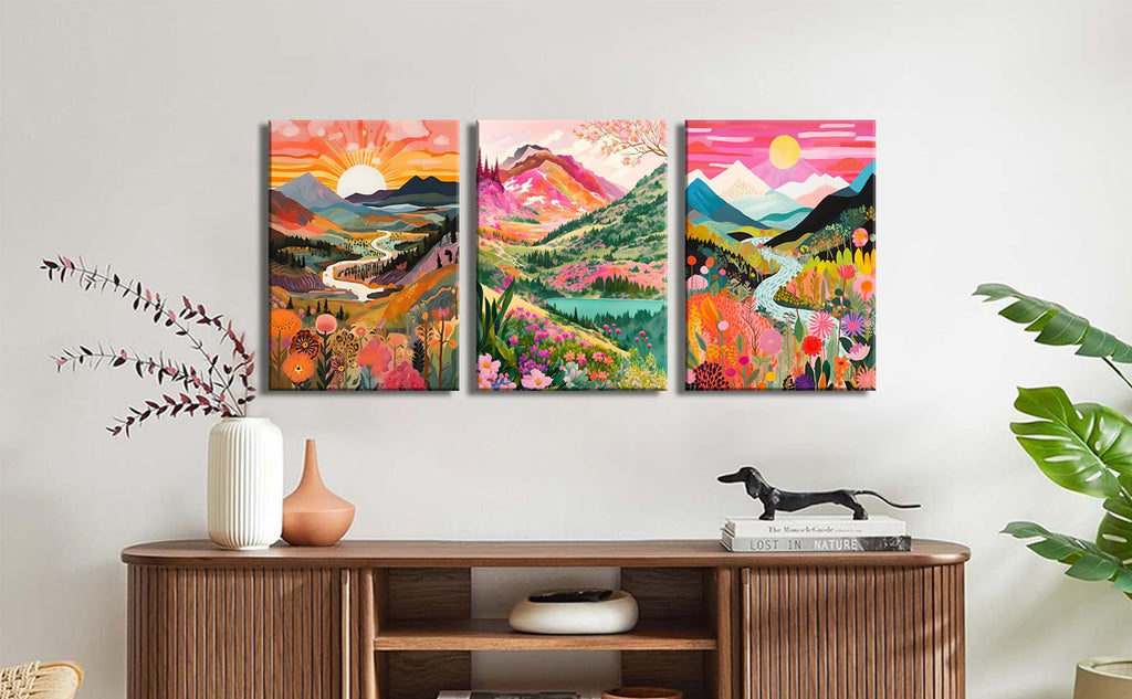 Three framed canvas prints of vibrant, abstract mountain landscapes with floral elements, displayed on a wall above a wooden cabinet.