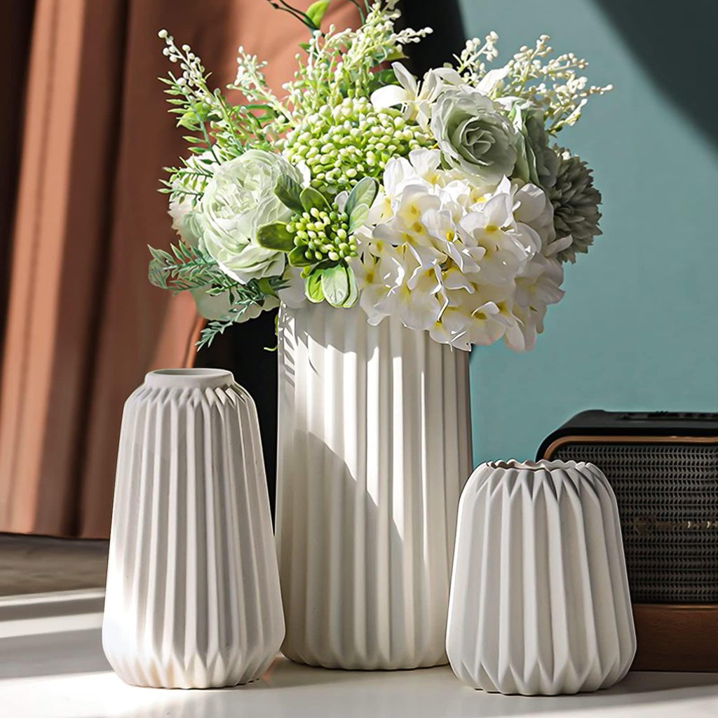 Three white ceramic vases with ribbed texture, one tall and two shorter, holding a bouquet of white and green artificial flowers.