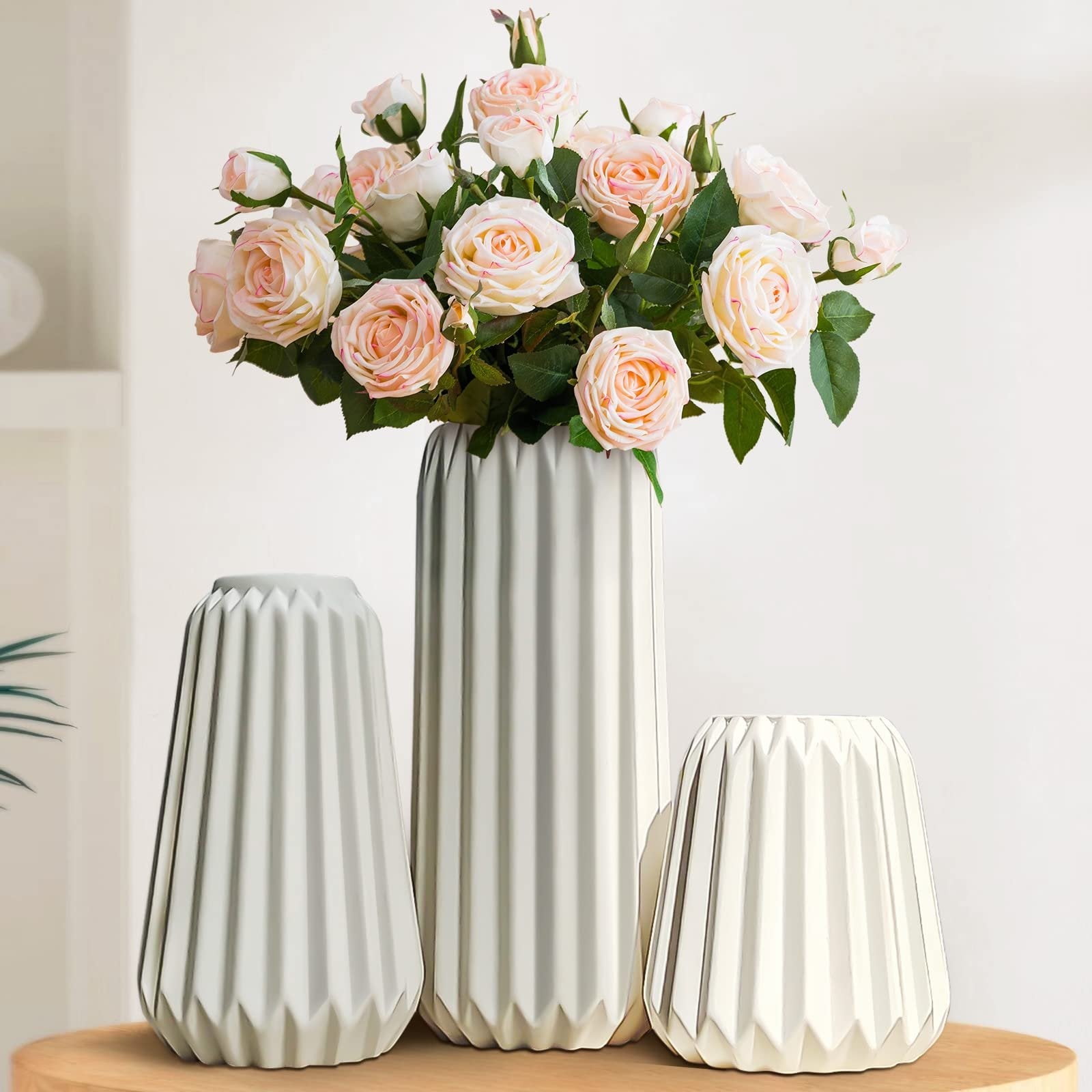 Three white ceramic vases with ribbed texture, one tall and two shorter, holding a bouquet of pink roses.