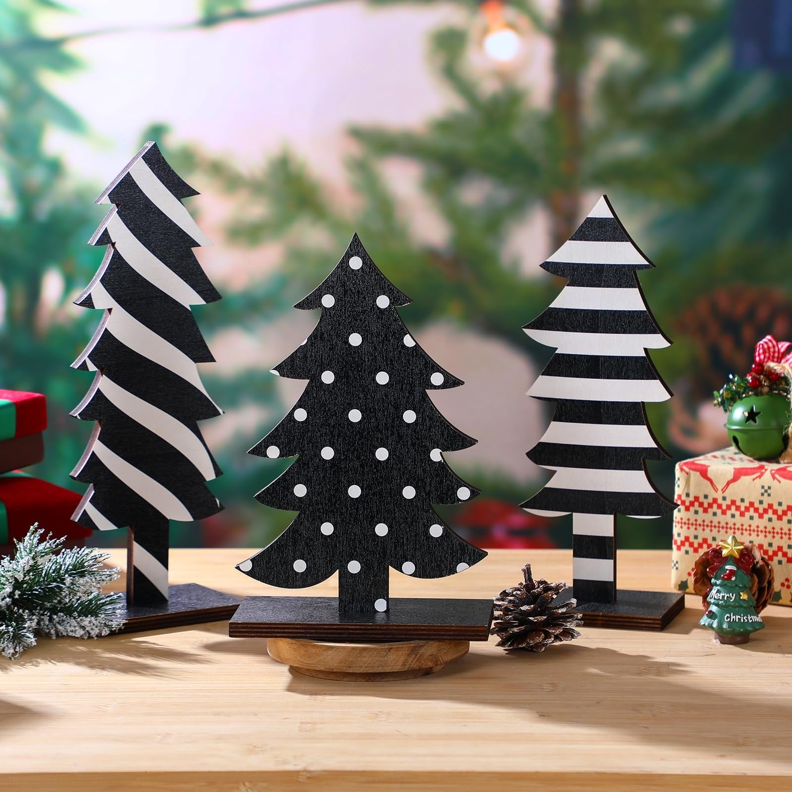 Three black and white wooden Christmas trees with different patterns on bases, arranged on a wooden surface with festive decorations.