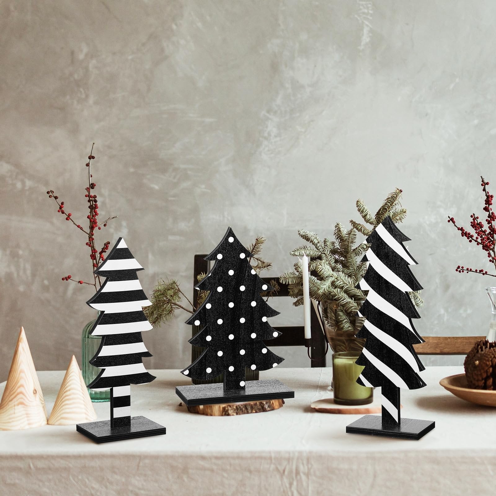Three black and white wooden Christmas trees with bases on a table, decorated with stripes and polka dots.