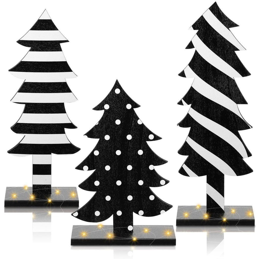 Three black and white wooden Christmas trees with bases and string lights, one with polka dots, two with stripes.
