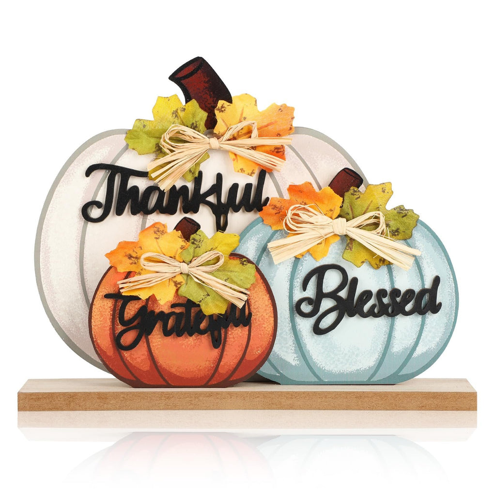 Three wooden pumpkins decorated with bows and autumn leaves, spelling "Thankful", "Grateful", and "Blessed".