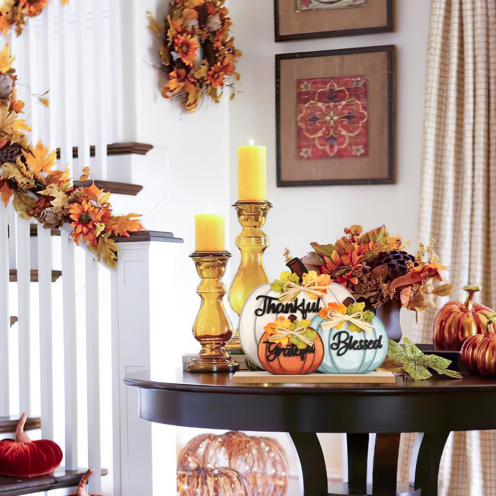 Three wooden pumpkins with fall decor, reading 'Thankful', 'Grateful', and 'Blessed', on a table with candles and a floral arrangement.