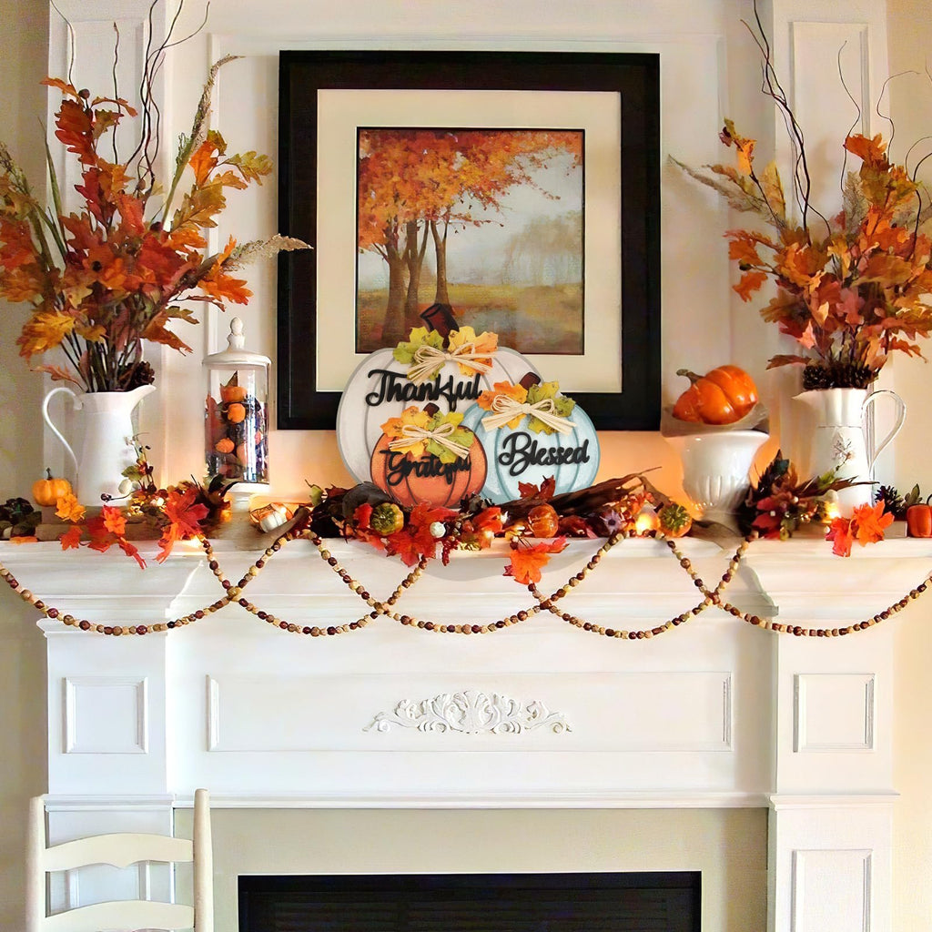 Three wooden pumpkins decorated with bows and maple leaves on a fireplace mantel with autumn foliage and a framed painting.