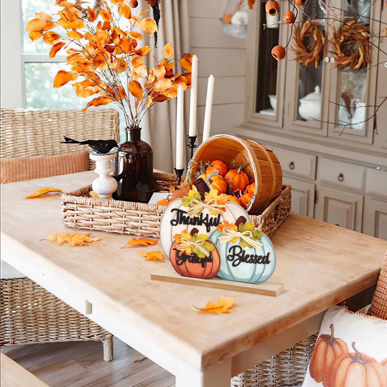 Three wooden pumpkins with fall sayings on a table, decorated with bows and leaves.