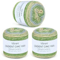 Three skeins of gradient cake yarn in green, cream, and blue hues, displayed against a white background.