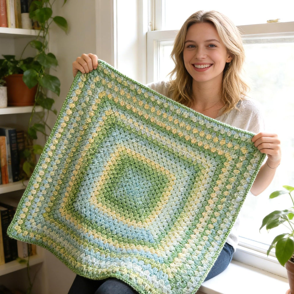 Smiling woman holding a crocheted blanket with green, blue, and yellow gradient pattern