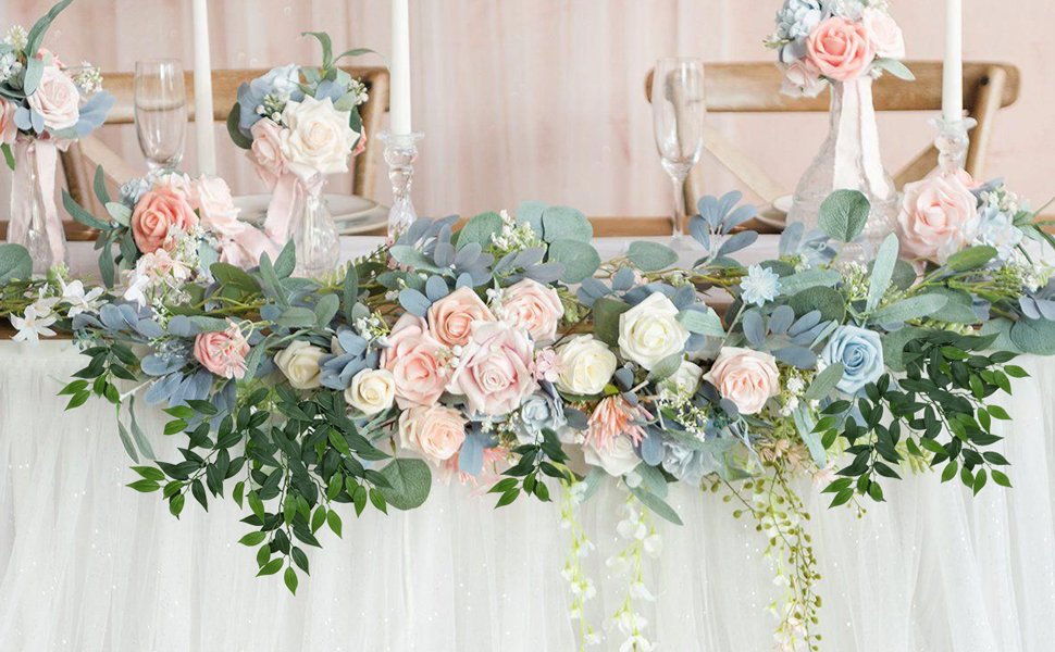Wedding table garland with pink, white, and blue roses and green leaves draped over a white tablecloth.