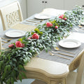 Silk Italian ruscus vine garland with pink roses draped across a table setting with plates and gold cutlery.