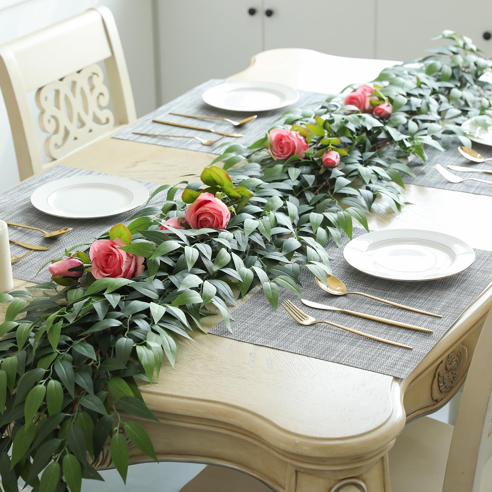 Silk Italian ruscus vine garland with pink roses draped across a table setting with plates and gold cutlery.