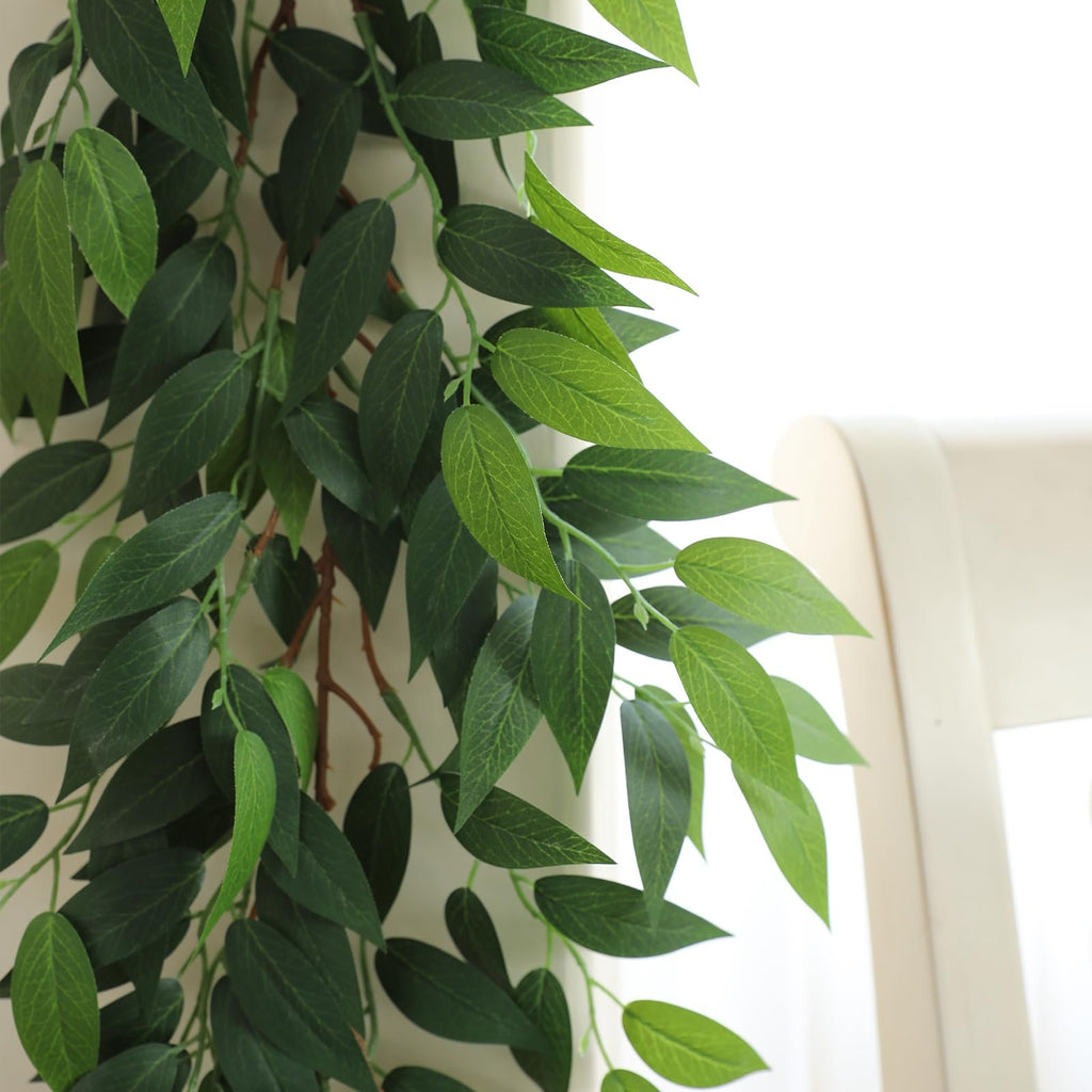 Close-up of a green silk Italian Ruscus vine garland with 100 leaves, draped against a white background with a cream-colored chair visible.