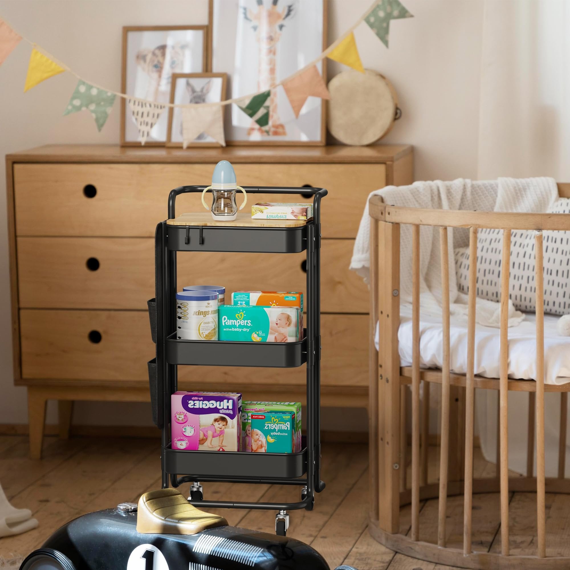 Black three-tier rolling cart with a wooden top, filled with baby products, in a nursery setting next to a crib.