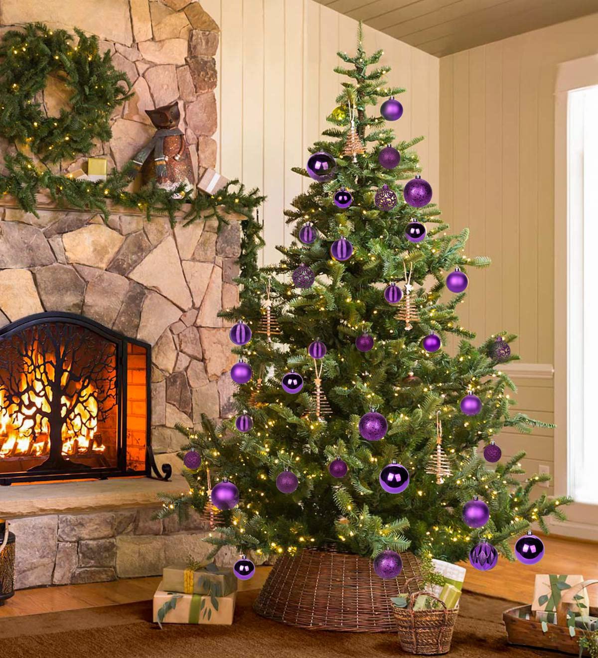 Decorated Christmas tree with purple ornaments and lights next to a stone fireplace with a fire