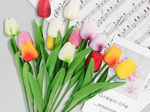Assortment of artificial tulips in various colors, including red, white, pink, yellow, and orange, arranged on a surface with sheet music and a magazine.