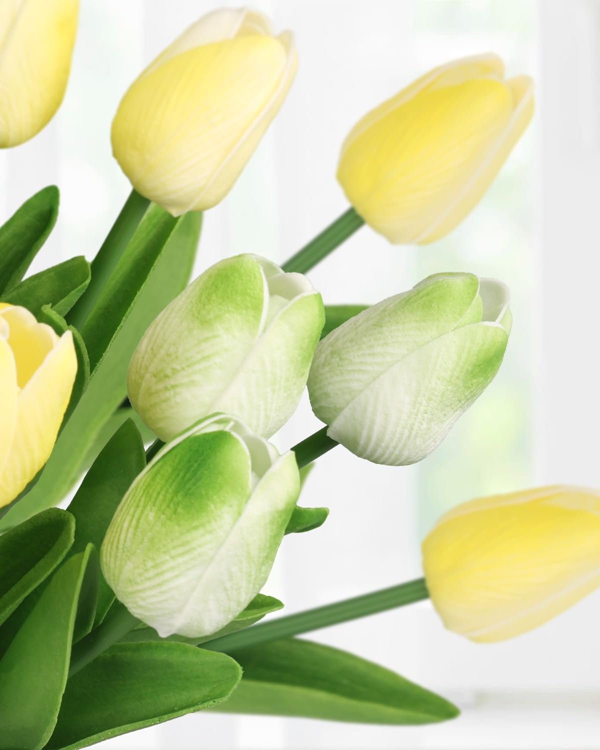 Close-up of yellow and green artificial tulip flowers with green leaves against a blurred white background.