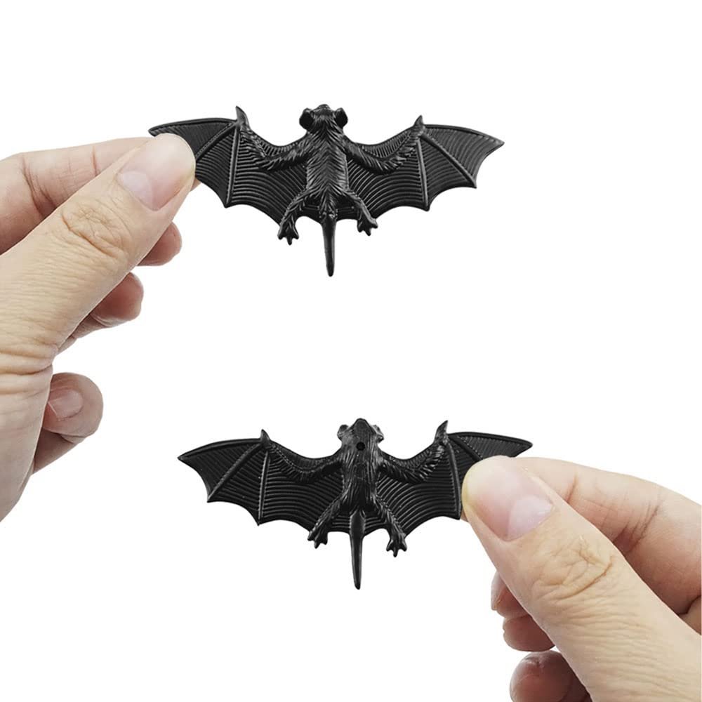 Two black plastic bat decorations held by hands against a white background