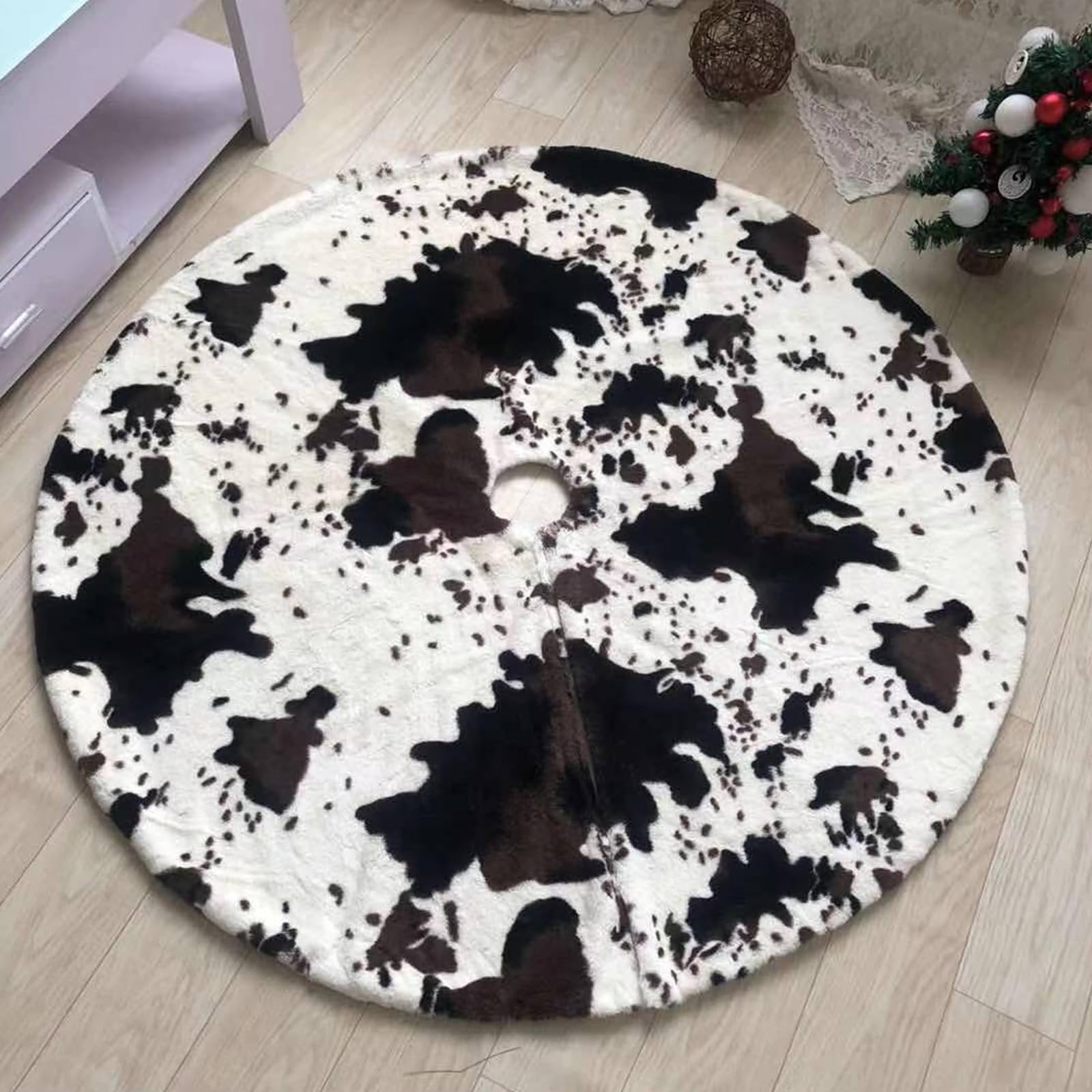 Round faux fur Christmas tree skirt with cow print pattern on a wooden floor.