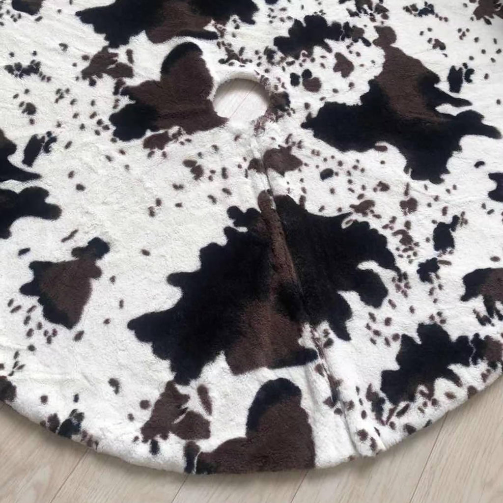 Close-up of a white and black cow print faux fur Christmas tree skirt with a hole in the center, laid on a wooden floor.