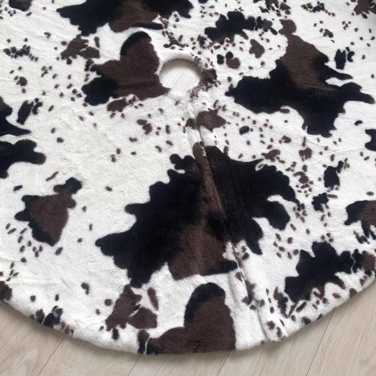 Close-up of a white and black cow print faux fur Christmas tree skirt with a hole in the center, laid on a wooden floor.