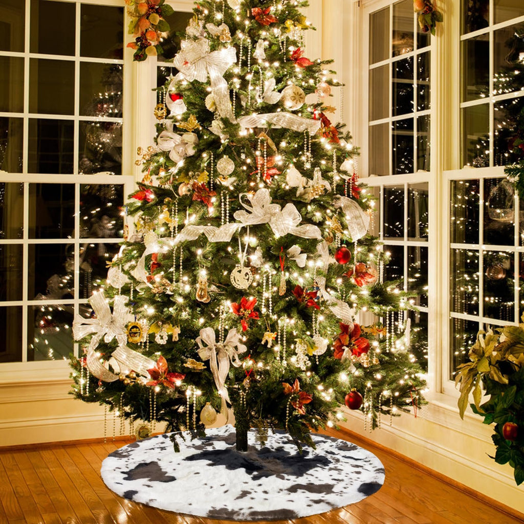 Decorated Christmas tree with cow print tree skirt in a room with large windows.