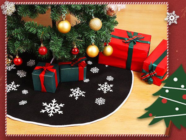 Black Christmas tree skirt with white snowflake print, placed under a decorated tree with gifts.