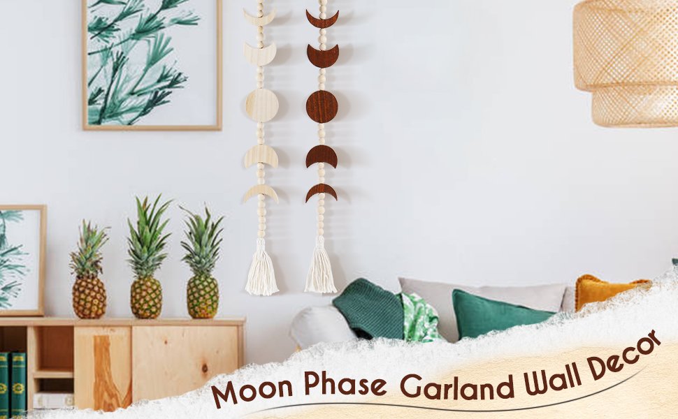 Two wooden moon phase garlands with beads and tassels hanging on a white wall above a wooden cabinet with pineapples.