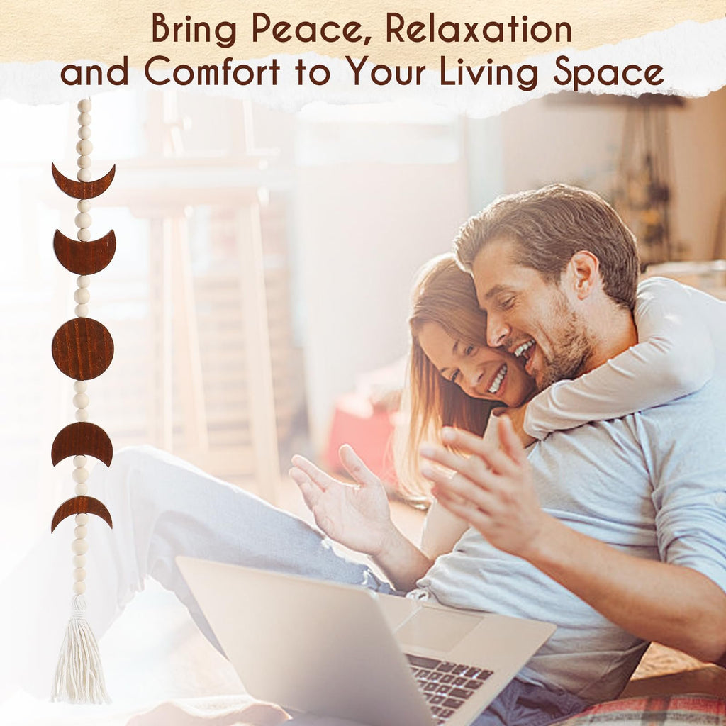 Wood moon phase wall hanging with beads and tassel, displayed in a living space with a couple using a laptop.