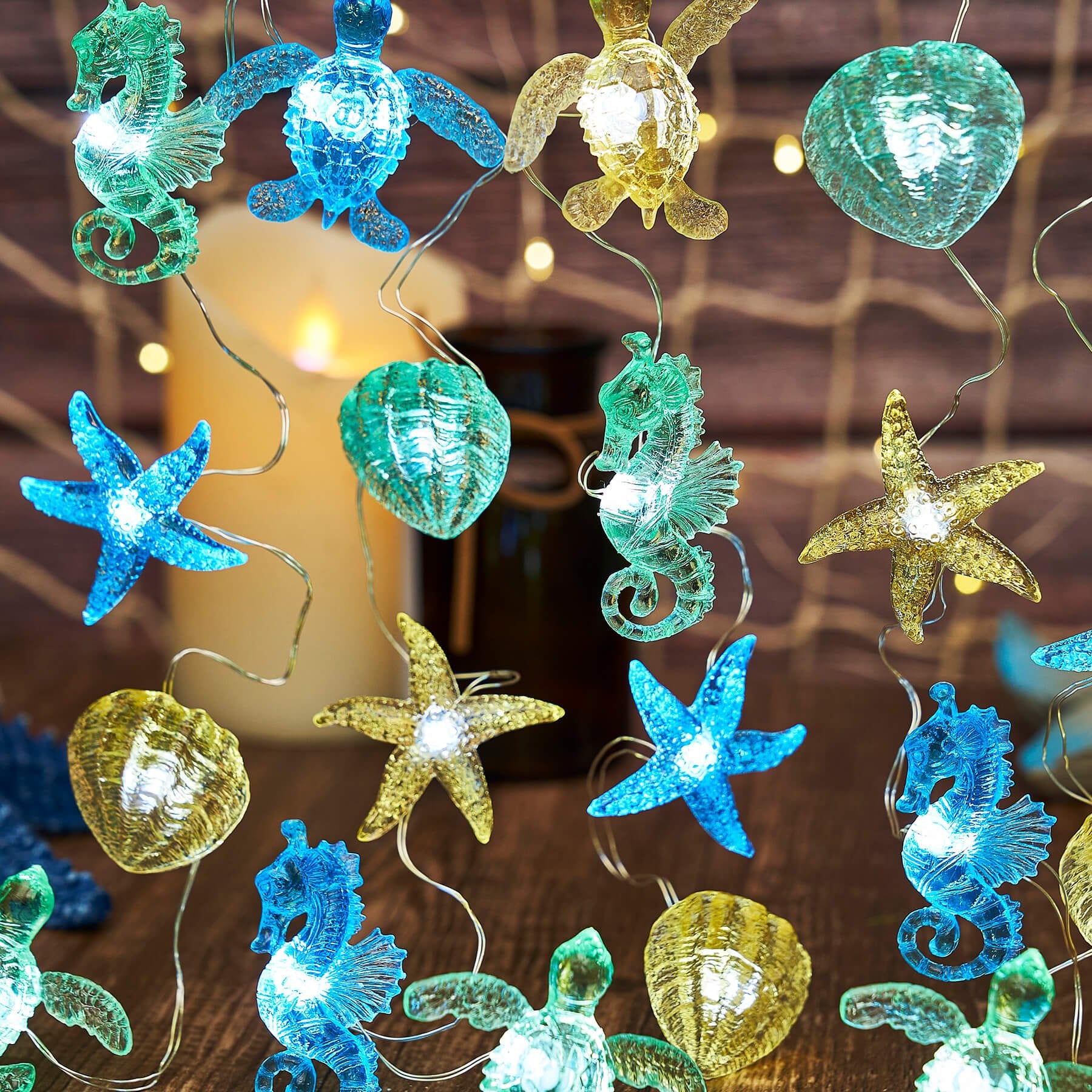 Nautical string lights with sea turtle, seahorse, starfish, and shell figurines on a wooden surface with a candle and net.