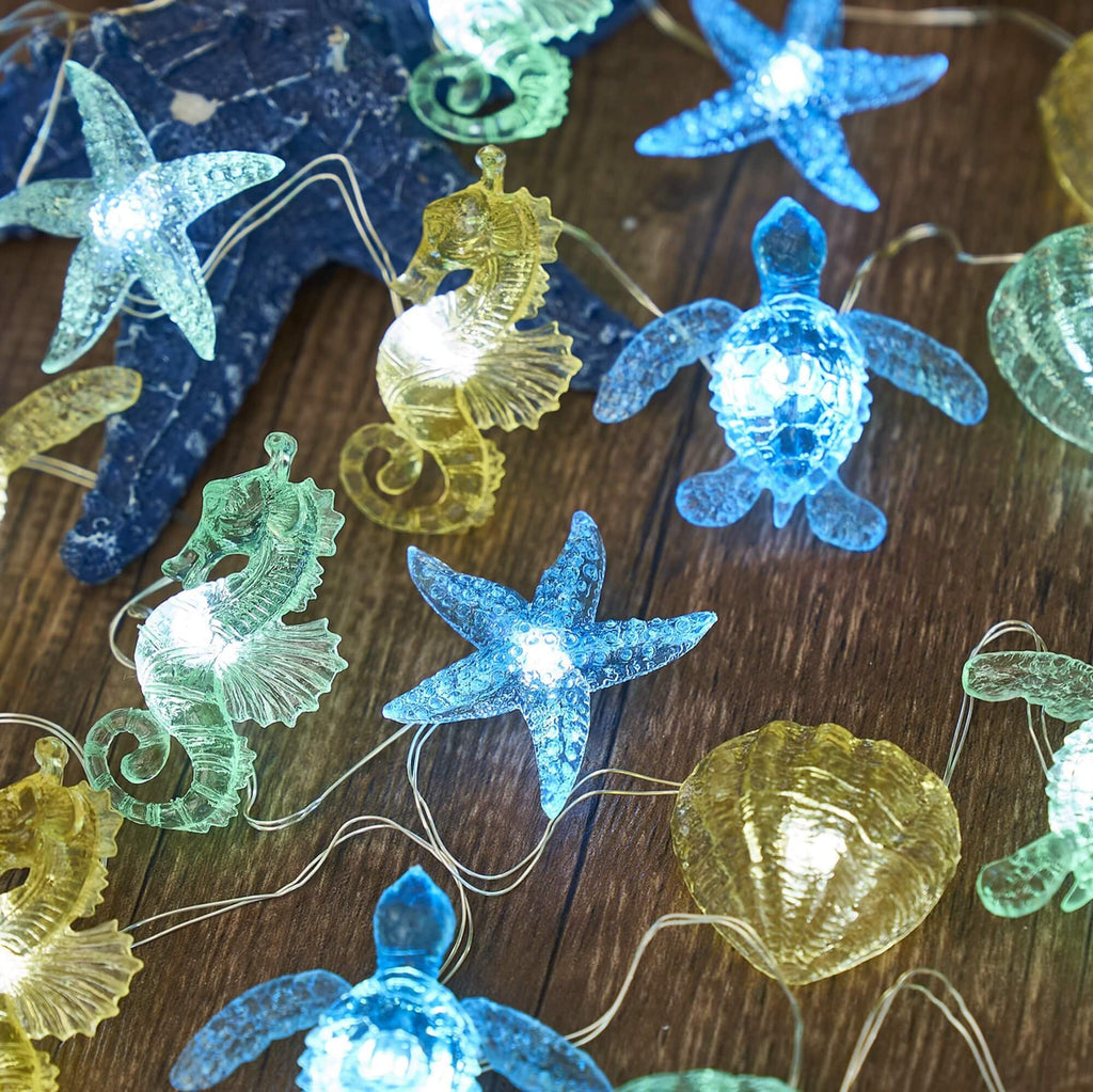 Nautical string lights with sea turtle, seahorse, starfish, and shell figurines on a wooden surface.