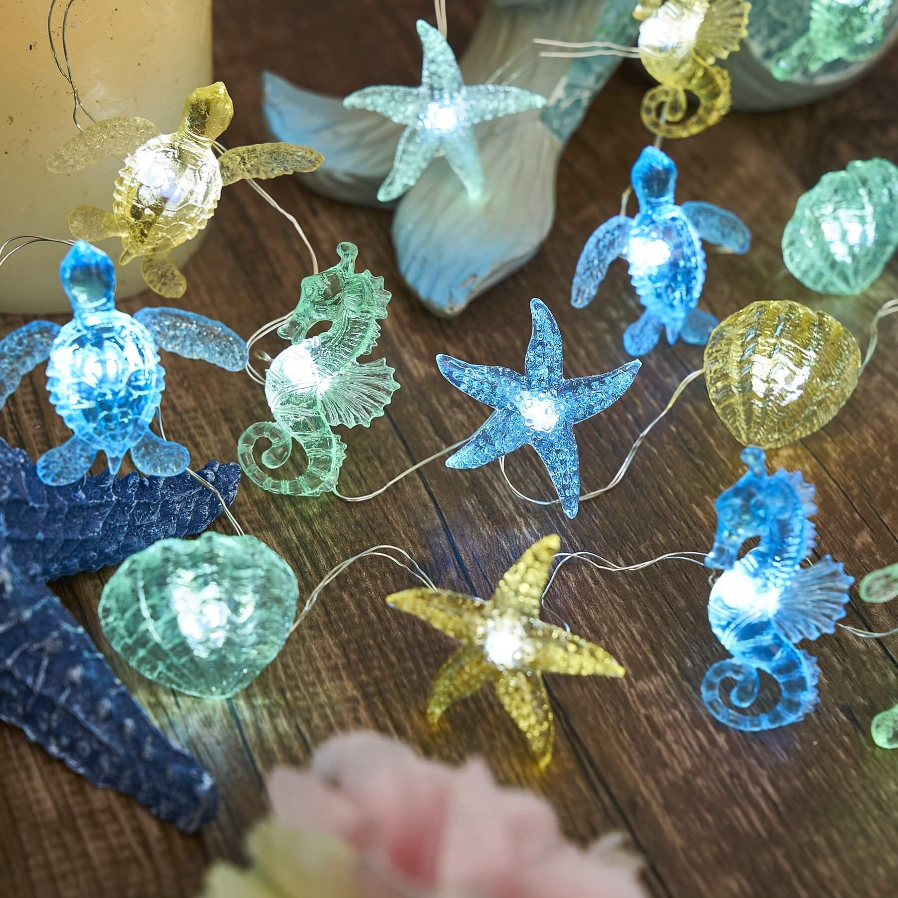 Nautical string lights with sea turtle, seahorse, starfish, and shell figurines on a wooden surface.