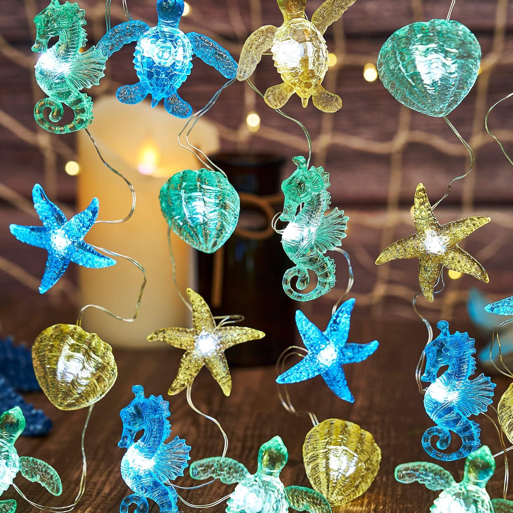 Nautical string lights with sea turtle, seahorse, starfish, and shell figurines on a wooden surface with a candle and netting.