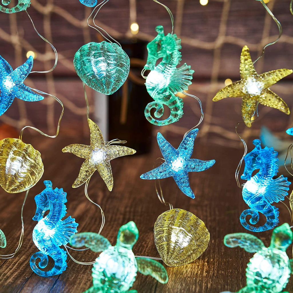 Nautical string lights with sea turtle, seahorse, starfish, and shell figurines on a wooden surface with bokeh lights.
