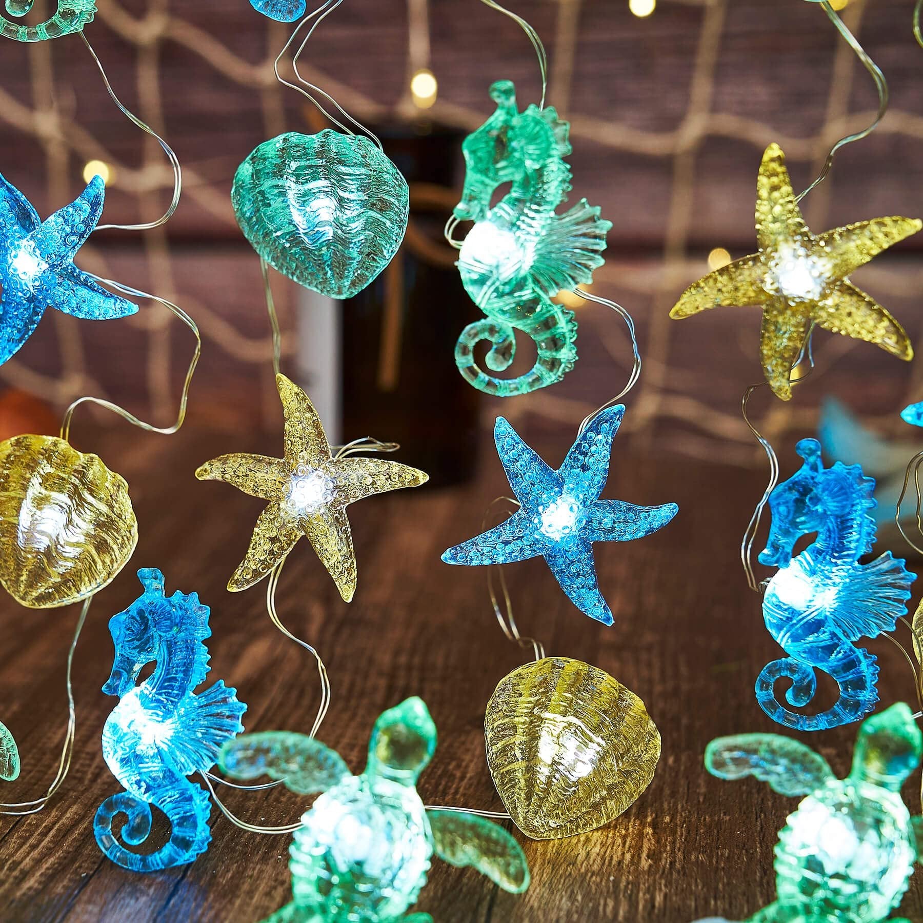 Nautical string lights with sea turtle, seahorse, starfish, and shell figurines on a wooden surface with bokeh lights.