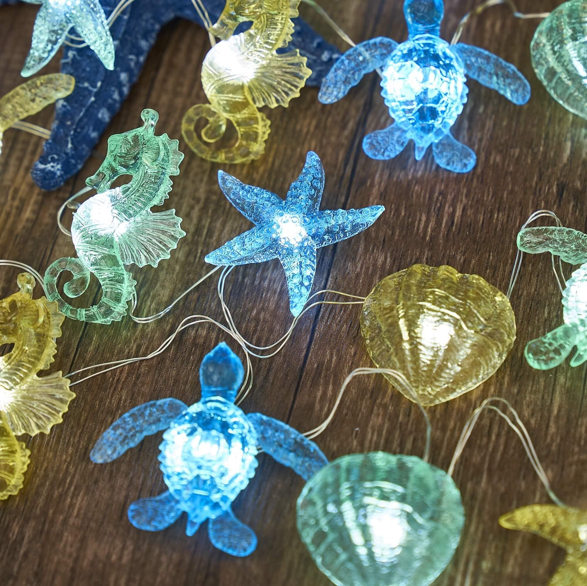 Nautical string lights with sea turtle, seahorse, starfish, and shell figurines on a wooden surface.