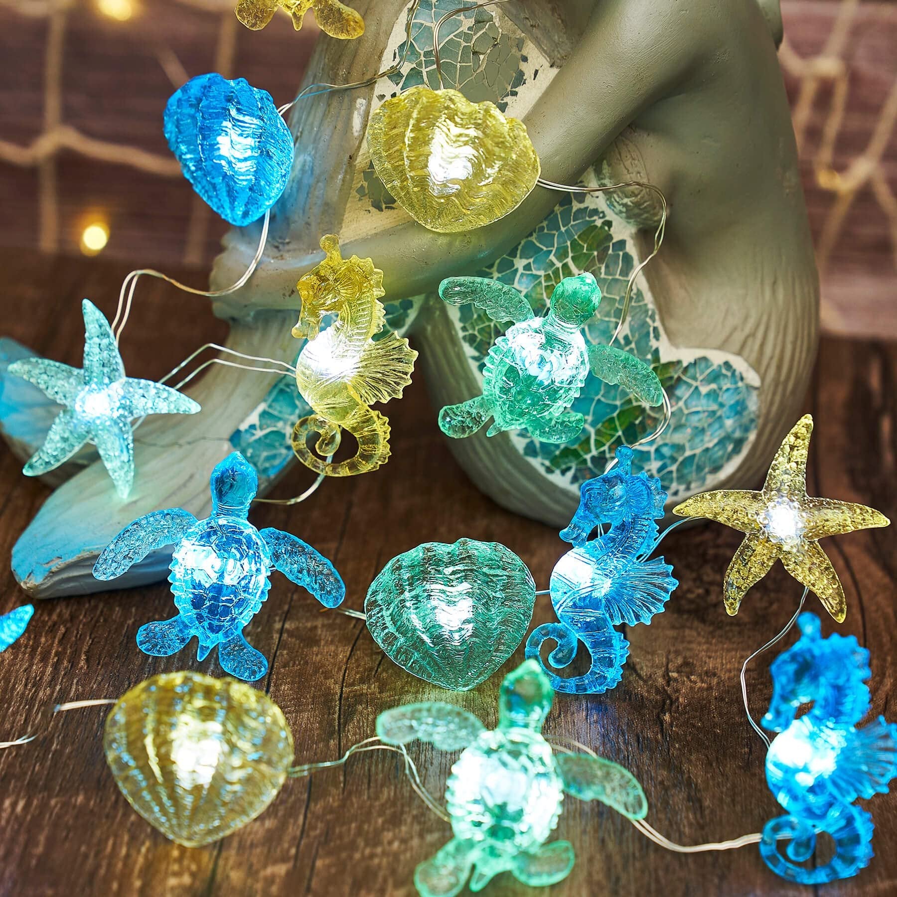 Nautical string lights with sea turtle, seahorse, starfish, and shell figurines on a wooden background.