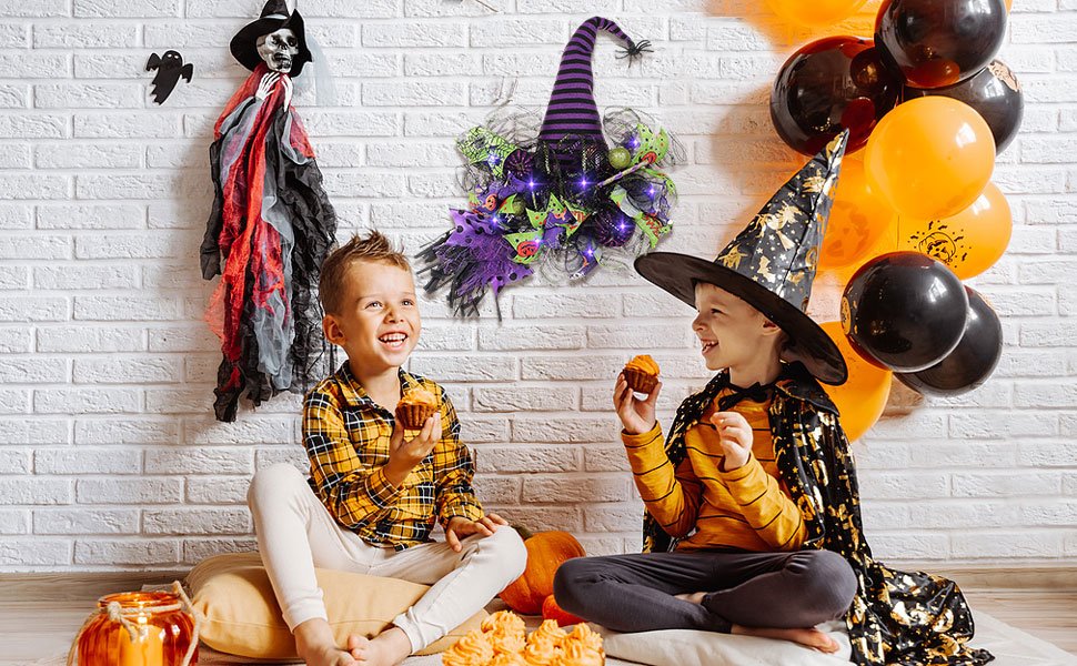 Two smiling boys in Halloween costumes eating cupcakes in front of a brick wall with decorations