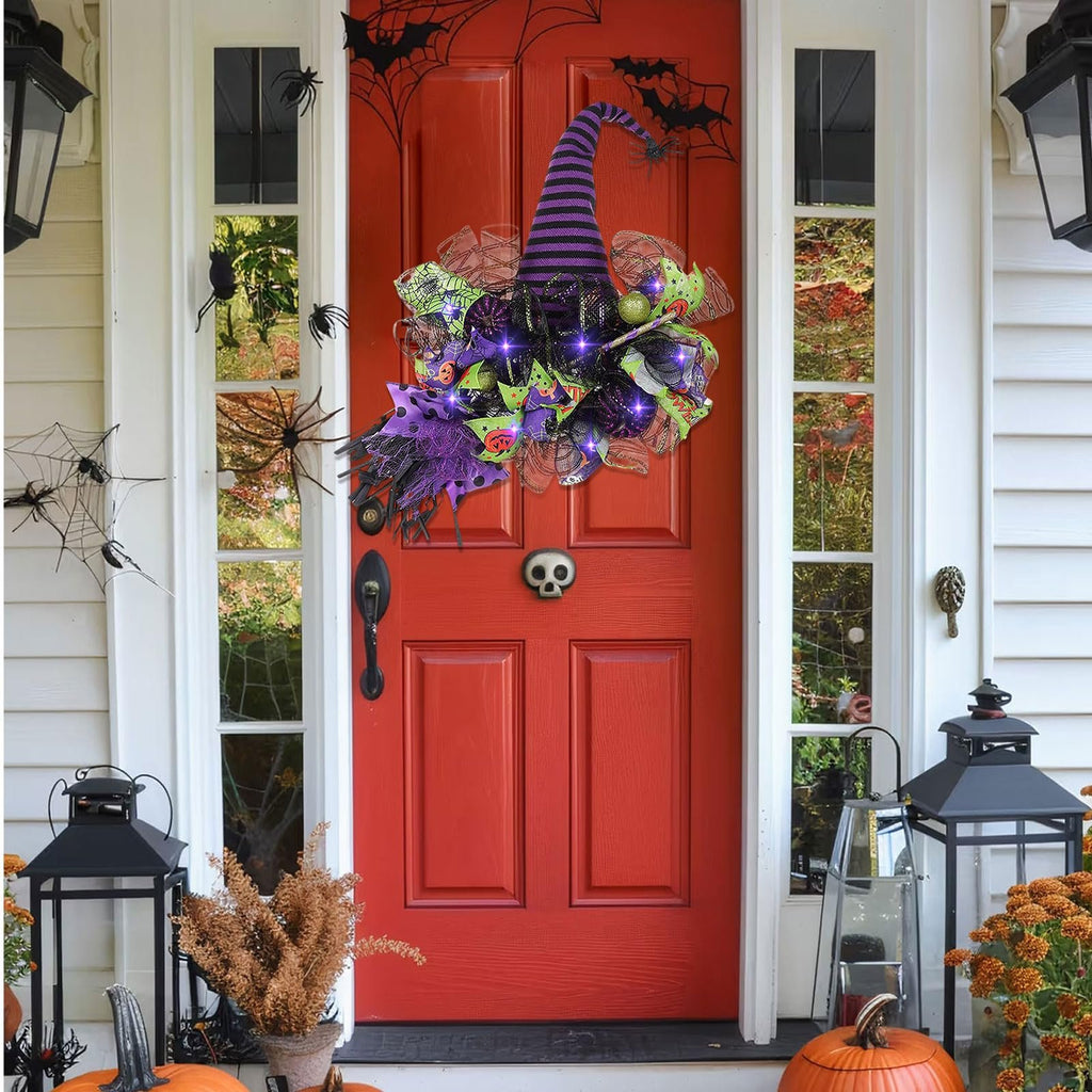 Halloween witch hat wreath with purple lights and mesh decor hanging on a red front door with spider web decorations.